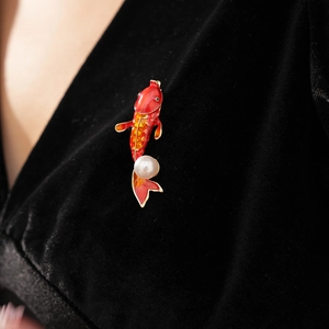 Close-up of a red koi fish brooch with white pearl on black velvet fabric