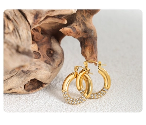 Detailed view of gold hoop earrings with pavé set zircon hanging on a rustic wood stand