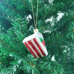 Red and white Christmas tree cake ornament hanging on a green festive branch