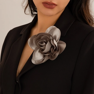 Detail of champagne rose brooch featuring multi-layered satin petals on a black suit