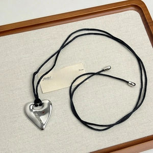 Macro detail of 3D silver heart pendant on black cord resting in a wooden jewelry tray