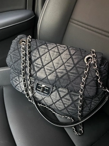 Macro detail of black denim quilted shoulder bag with silver chain on leather seat