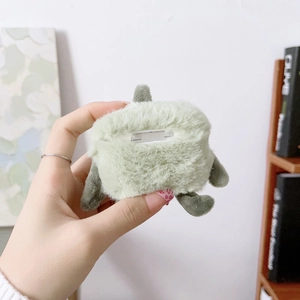 Close-up of green plush monster case for AirPods held by hand showing soft fur texture