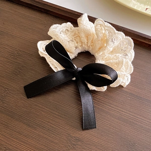 Détail macro du chouchou en dentelle avec nœud en satin noir sur plateau en bois