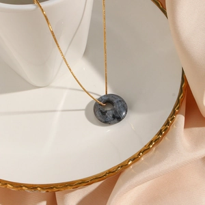Close-up of a dark grey round stone pendant necklace on a decorative white gold-rimmed plate