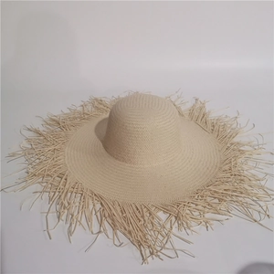 Detail of hand-woven straw sun hat showing natural beige fibers and frayed fringe brim