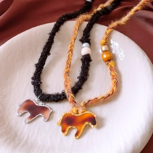 Detail of woven necklaces with amber resin pony pendants and wooden beads on white ceramic