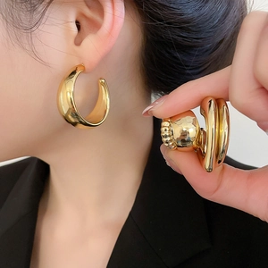 Detail of large polished gold C-shape hoop earrings showing metallic reflection