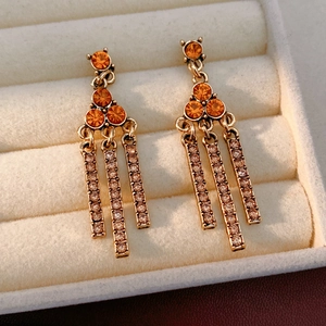 Close-up of golden tassel earrings with orange gemstones in a beige velvet jewelry box
