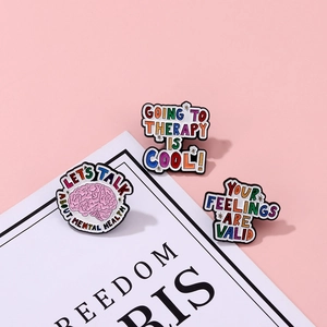 Macro detail of rainbow enamel mental health pins on a soft pink decorative background
