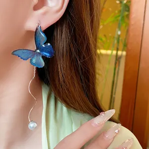Blue butterfly drop earrings with long silver wavy chains and pearls on female model