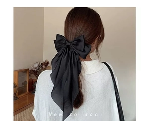 Detail of a large black satin bow hair clip with long streamers on styled hair