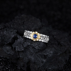 Macro detail of silver ring with golden flower and blue gemstone on black rock