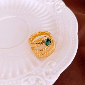 Detailed macro view of gold-plated snake ring with green teardrop zircon on a vintage plate