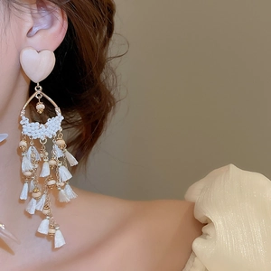 Close-up of elegant wooden heart earrings with long white tassels and golden accents