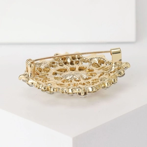 Back view of vintage golden oval rhinestone brooch with hollow metal design on white base