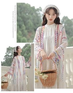 Dettaglio del cardigan traforato bianco con bordo geometrico colorato e nappe