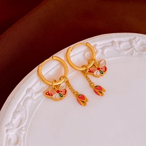Detailed macro of matte gold butterfly earrings with enamel flower on vintage dish