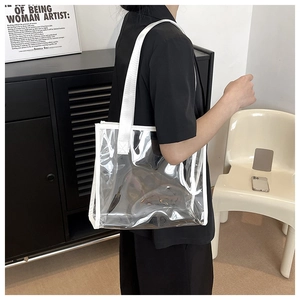 Detail of a clear PVC tote bag with white trim shown on a model in a minimalist setting