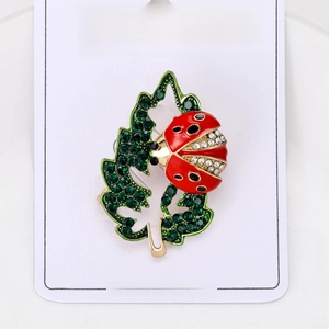 Macro detail of leaf and ladybug brooch with red enamel and sparkling green rhinestones