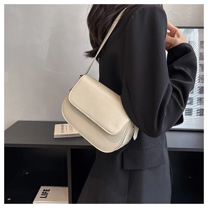 Detail of minimalist cream crossbody saddle bag worn by a model in a black blazer