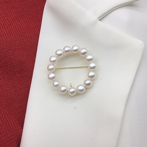 Detailed close-up of a round white pearl brooch with gold base on a blazer lapel