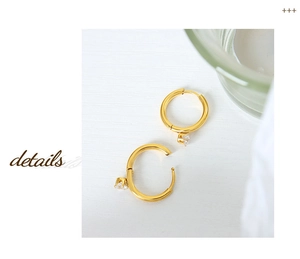 Detail of gold circular earrings featuring a sparkling clear zircon on a white wood surface