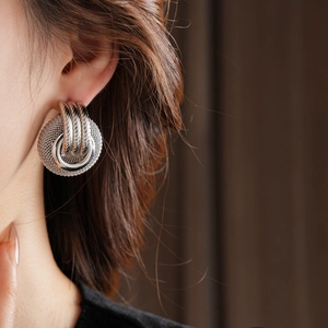 Close-up of woven silver metal double-loop earrings worn by a model in soft lighting