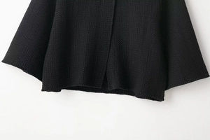 Detailed close-up of premium black knit fabric texture and hem stitching on cardigan