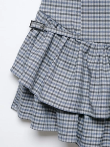 Detail of grey plaid dress featuring double-layered ruffles and silver buckle belt