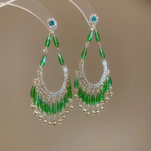 Détail de boucles d'oreilles fleuries avec pampilles émeraude et accents dorés sur support