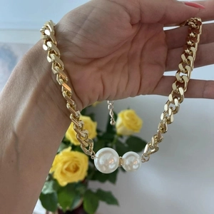 Detail of gold chunky chain necklace featuring two white faux pearls and adjustable clasp