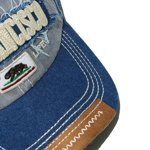 Close-up of distressed denim baseball cap with bear embroidery and contrast stitching