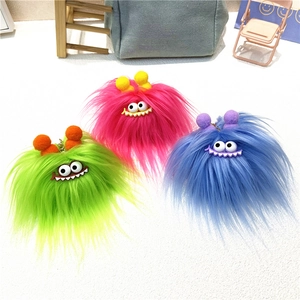 Three colorful fuzzy monster keychains with big eyes and pom-poms on a white table