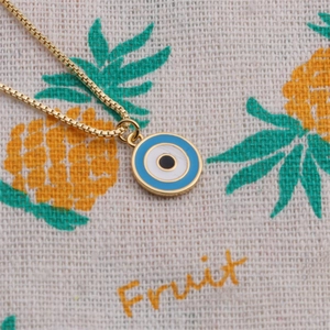 Golden box chain necklace featuring a blue enamel evil eye pendant on fruit pattern cloth