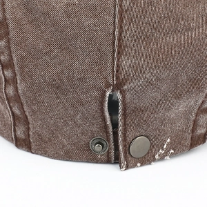 Détail du tissu denim délavé marron avec boutons-pression en métal et coutures usées