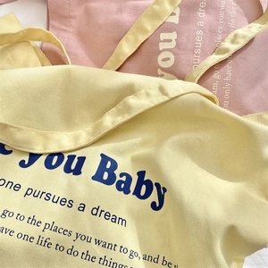 Detail of printed canvas tote bags in pastel yellow and pink showing woven fabric texture