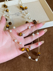Detailed view of layered necklace with tiger eye beads and pearls on gold chains