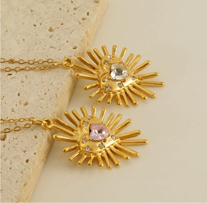 Gros plan de colliers cœur soleil dorés avec zircons clairs et roses sur fond pierre