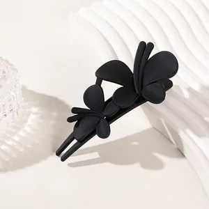 Detail of matte black butterfly duckbill hair clip on a white textured display stand