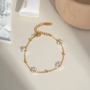 Détail d'un bracelet en acier inoxydable doré orné de cinq fleurs en perles blanches