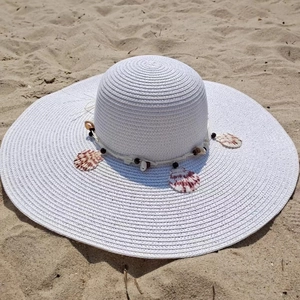 Detail of white straw sun hat with seashell and bead accents on beach sand