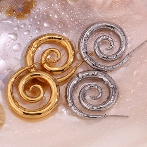 Macro shot of gold and silver spiral earrings with water droplets on shell background