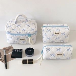 Three-piece set of white quilted cosmetic bags featuring a blue bow pattern and zip closure