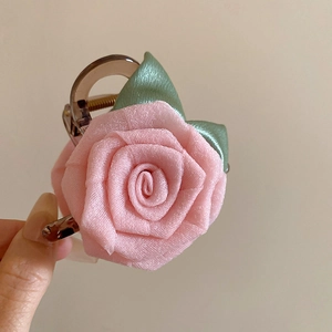 Détail d'une pince à cheveux avec une rose en tissu rose et feuilles vertes en main