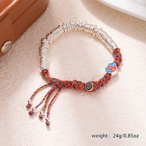 Detail of hand-woven bracelet with enamel charm and metal beads on beige background