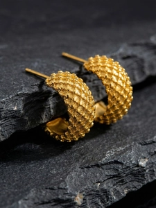 Macro shot of gold-plated C-shaped earrings with textured beads on a black rock surface