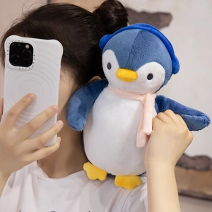 Detail showing the plush penguin toy with a pink scarf and blue earmuffs in a lifestyle setting