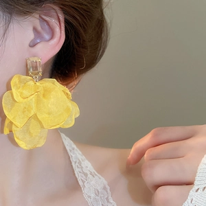 Close-up of yellow fabric flower earring with a crystal center on a female model