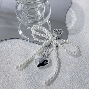 Cute faux pearl bow bag charm with a polished silver heart pendant and metal clasp